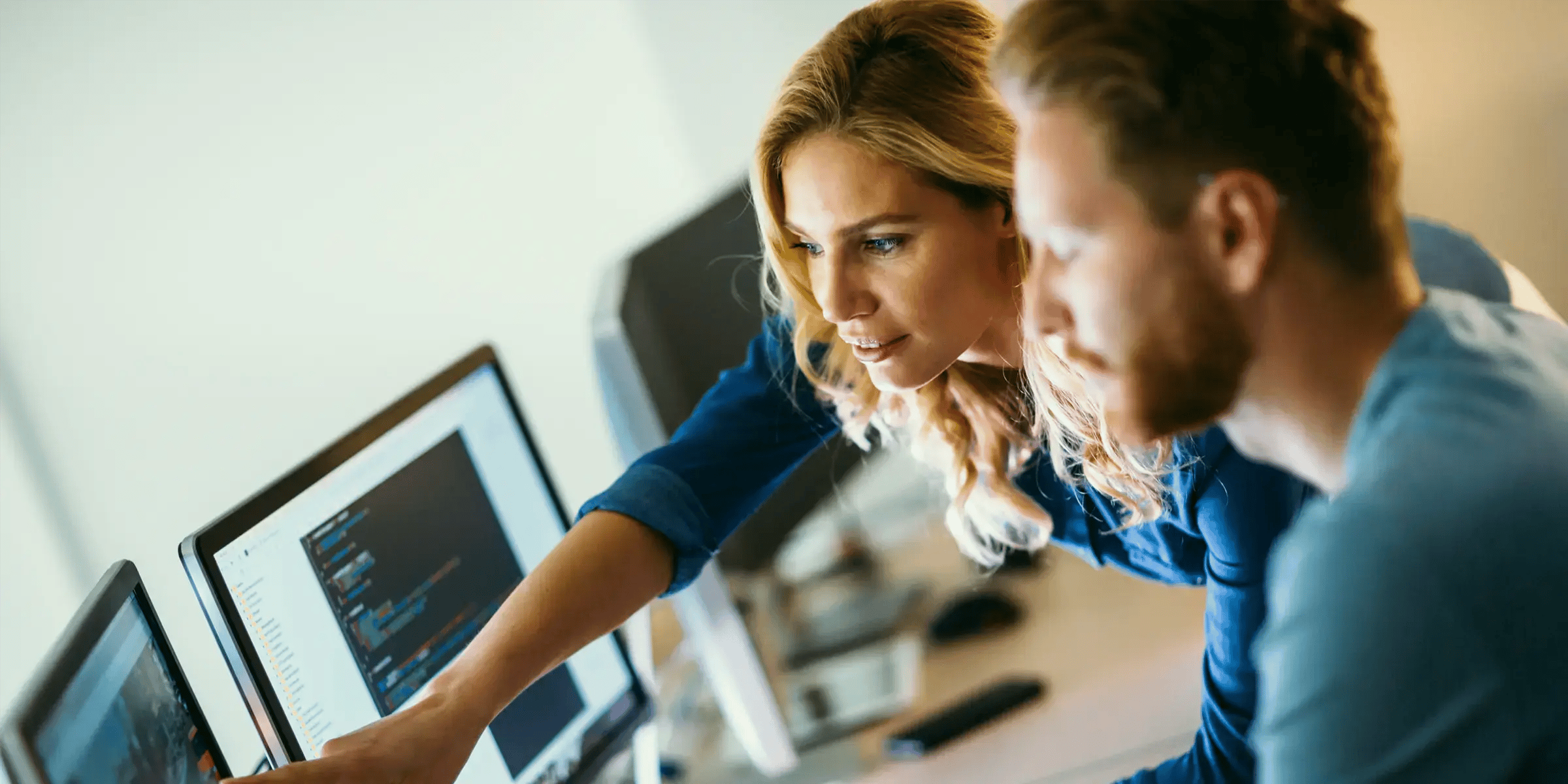 A man and woman working in front of two screens
