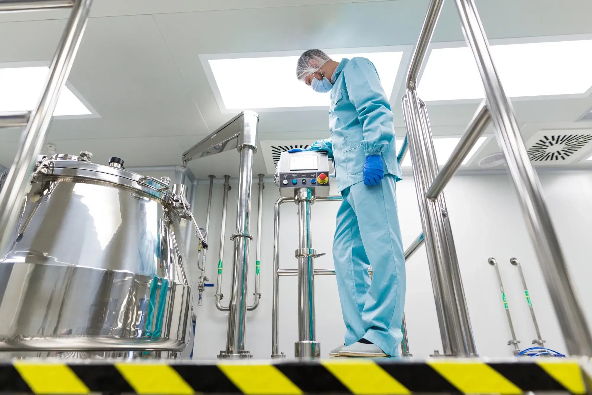 caucasian-scientist-blue-lab-suit-gloves-configure-control-panel-near-steel-tank-look-panel-black-yellow-stripes