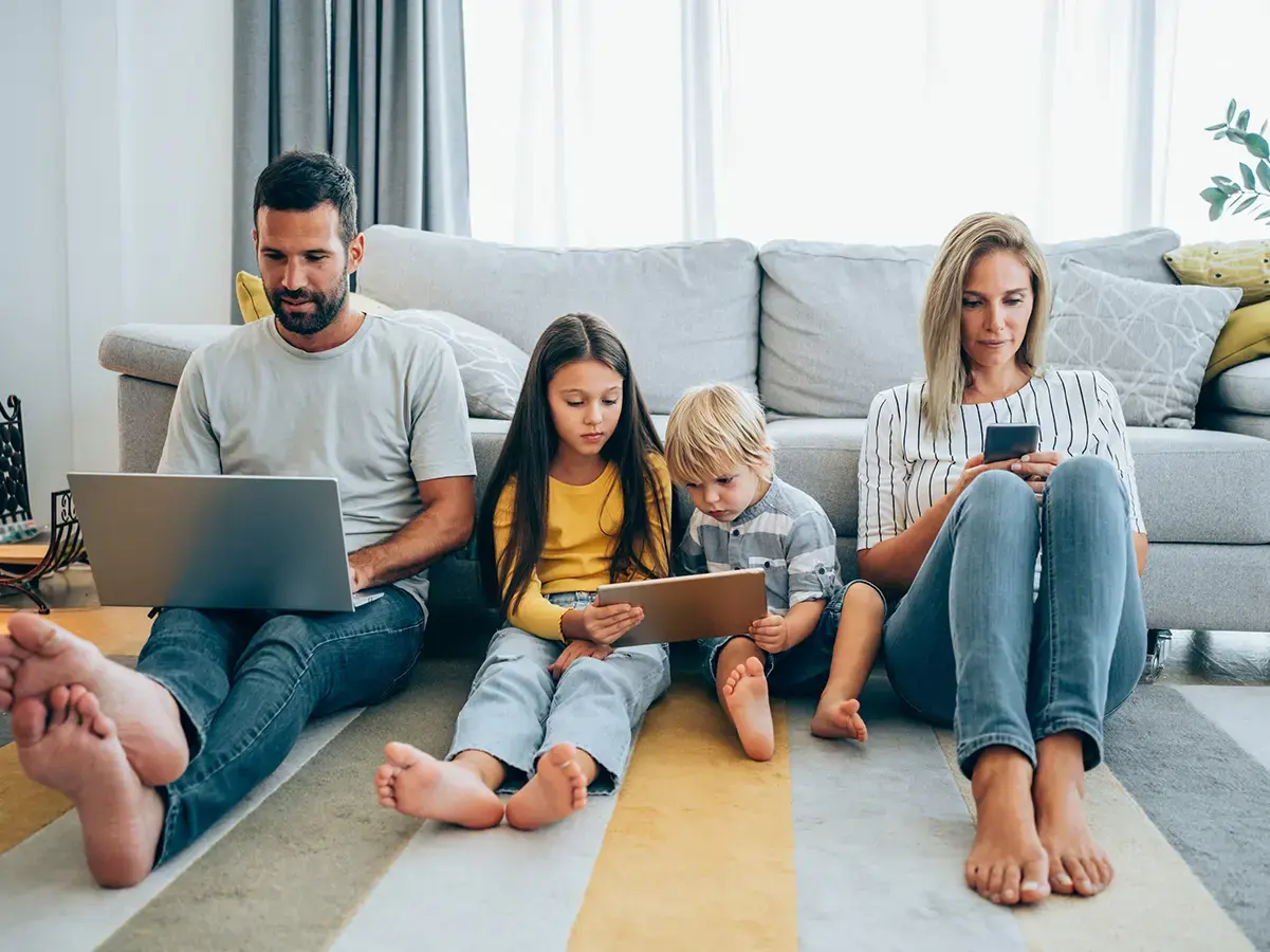 A family with two adults and two kids browsing different digital devices at home