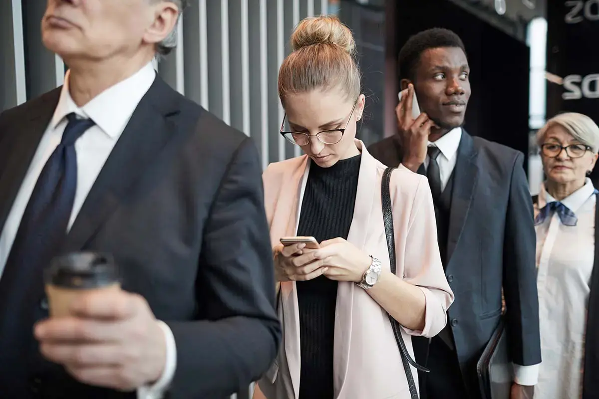 Professionals in an airport queue working on their mobile phones
