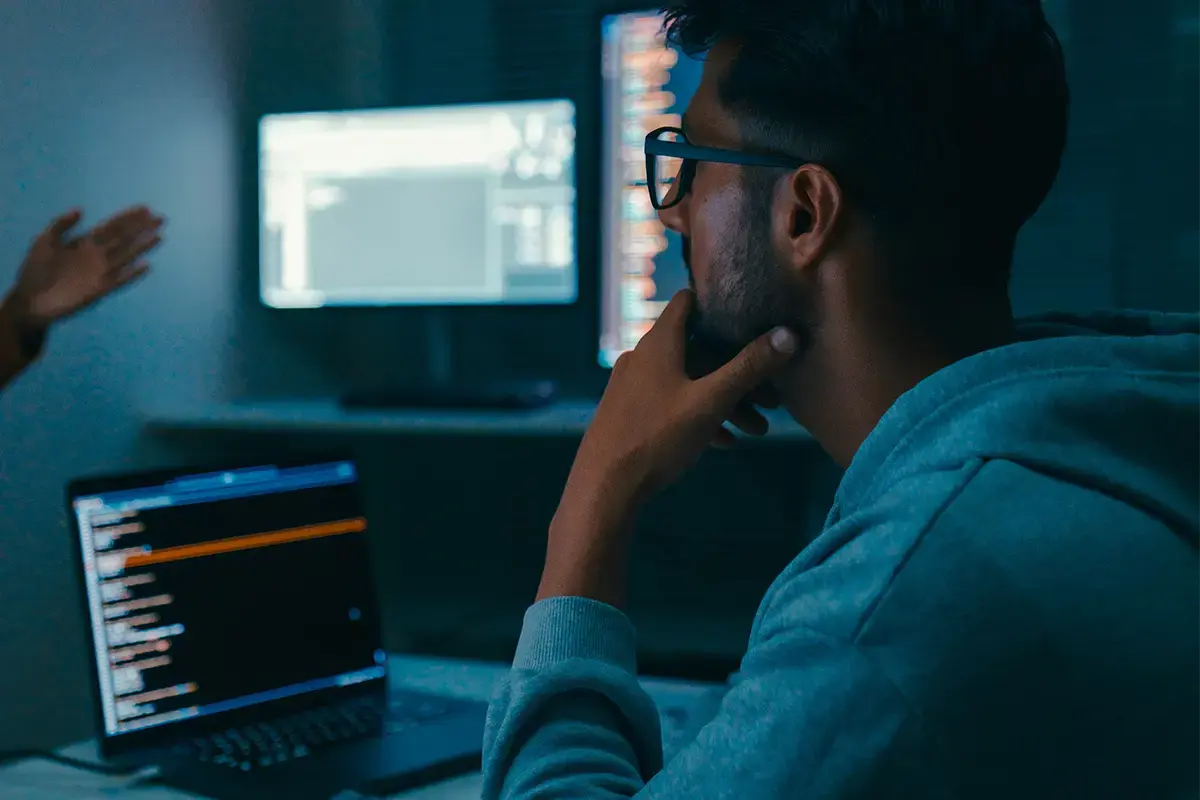 A telecom engineer in working with coding on his laptop and talking to a colleague