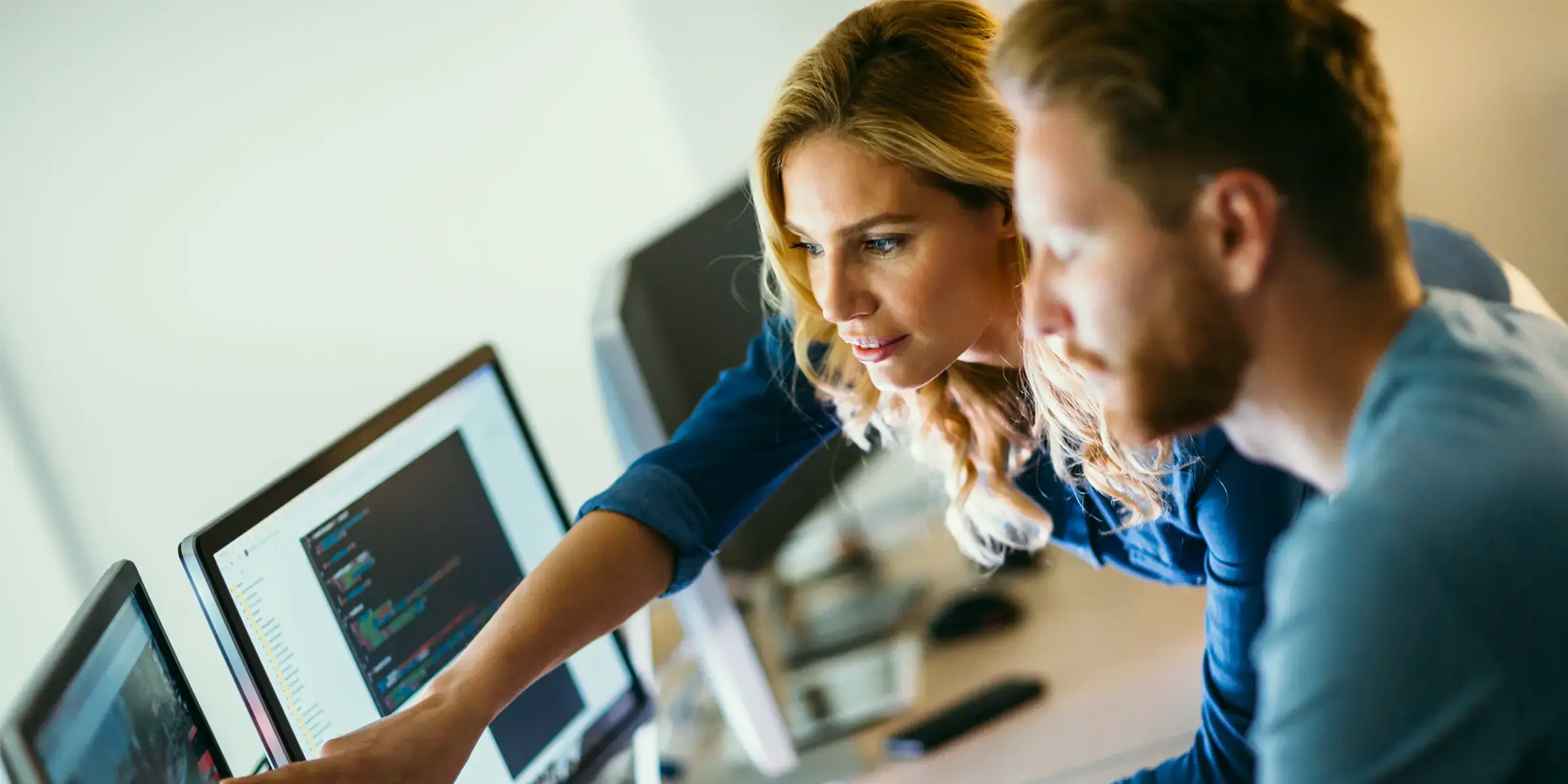 A man and woman working in front of two screens